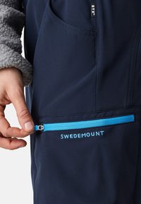 Navy outdoor jacket featuring a light blue zippered pocket. Soft gray fleece sleeves and a logo reading "SWEDEMOUNT" are visible.