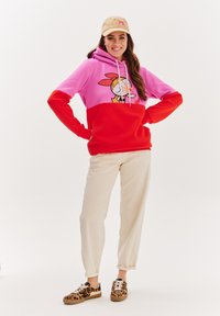 Světlá mikina s růžovou horní částí a červenou dolní částí, s designem karikaturní postavy. Spárována se krémovými kalhotami a botami s leopardím vzorem.