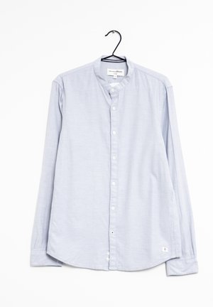 Camisa de manga larga azul claro con cuello mandarín y botones blancos, colgada en una percha negra contra un fondo blanco.