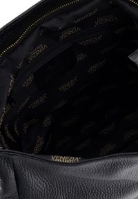 Interiér černé kožené kabelky s kapsou na zip. Podšívka z tmavé tkaniny s opakujícím se vzorem zlatého loga "VENEZIA". Zlatý detail zipu.