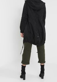 Czarna kurtka z kapturem, z długimi rękawami, ściągnięta w talii i o luźnym kroju. Połączona z oliwkowymi spodniami cargo i czarnymi botkami na obcasie.