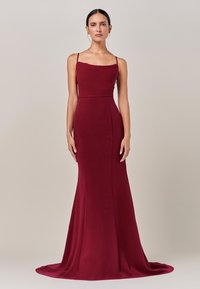 Burgundska večernja haljina s pripijenim gornjim dijelom, tankim naramenicama i suknjom koja se širi, izrađena od glatkog materijala sa suptilnim sjajem.