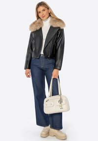 Giacca nera in ecopelle corta con un colletto in ecopelle beige, abbinata a un dolcevita bianco, jeans a gamba larga blu e una borsa color crema.