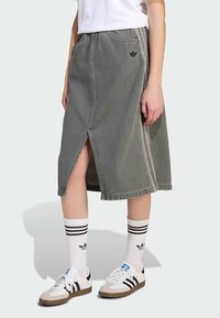 Denim midikjol i blekt grått med slits fram, med kontrasterande sidostrippar och en broderad logotyp vid midjan. Kombinerad med sneakers.