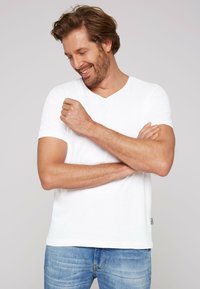 White cotton t-shirt with a v-neck and short sleeves, paired with light blue denim jeans. Soft texture and relaxed fit.