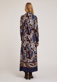 Rochie lungă, cu model maro, decorată cu un design floral albastru, cu mâneci lungi și o fustă lungă. Prezintă manșete decorative și o siluetă ajustată.