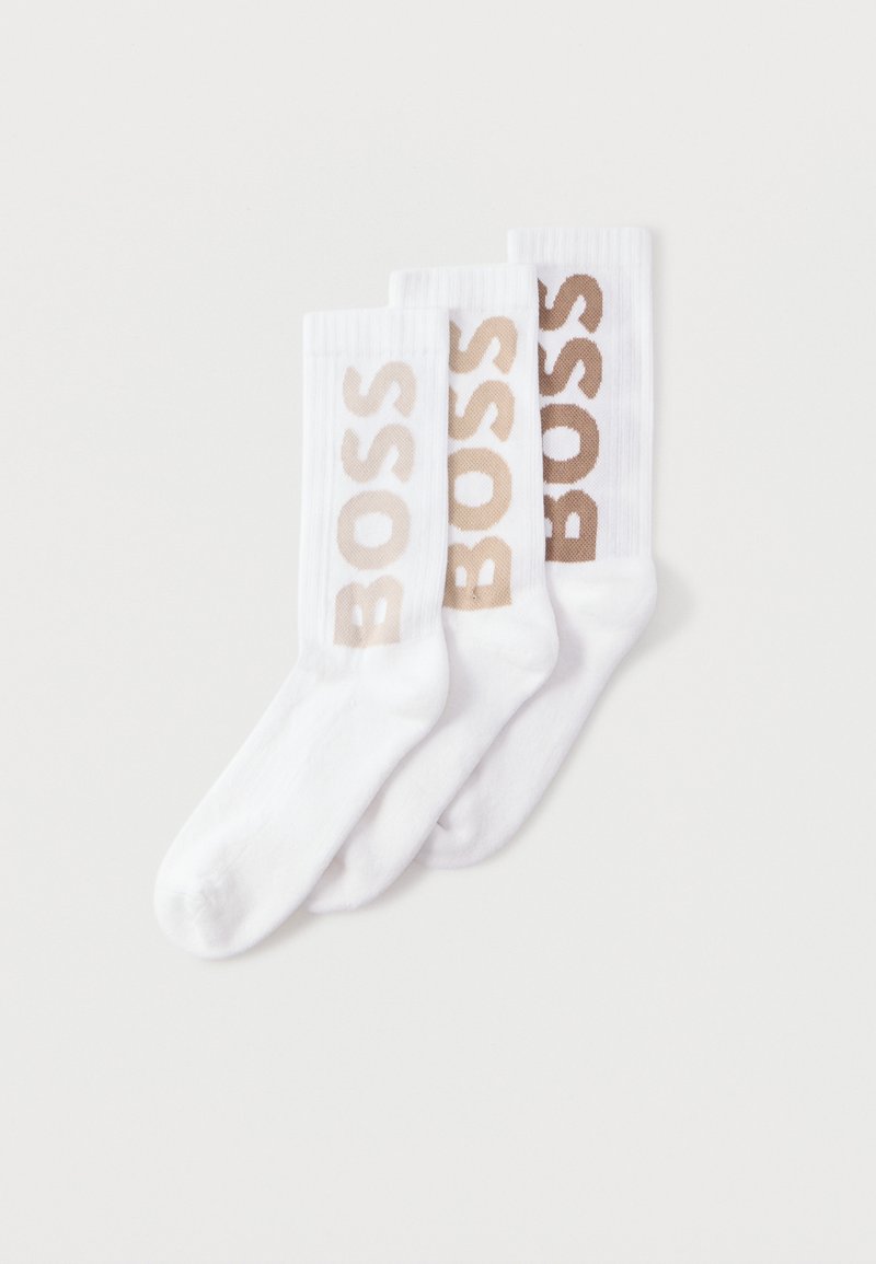 Trois paires de chaussettes blanches montantes avec des bords côtelés, chacune arborant le mot "BOSS" en lettres beiges sur le côté.