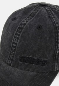 Gorra de denim negra con tejido texturizado, costuras en tono y un logotipo bordado de "GUESS" en la parte frontal, que presenta un visor curvado clásico.