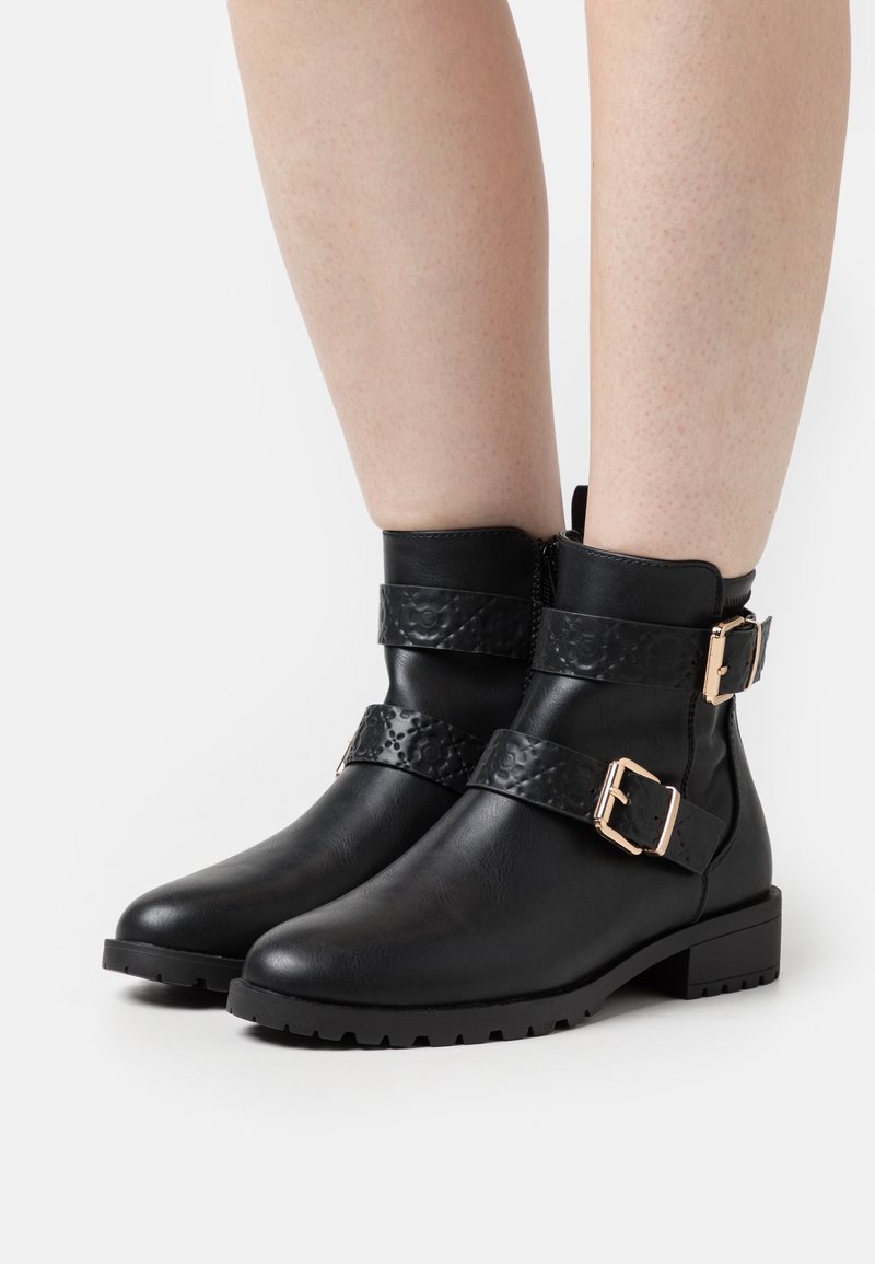 Botas negras hasta el tobillo con una correa texturizada, hebillas y una suela plana. Presentan un acabado de cuero liso y una suela exterior resistente y con tacos.