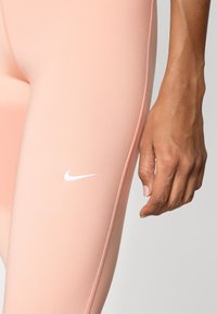 Pink athletic leggings with a smooth texture, featuring a white Nike logo near the bottom hem and a fitted design.