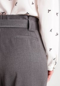 Szare spodnie z teksturowanej tkaniny, szerokim pasem i tylnymi kieszeniami, w połączeniu z białą bluzką z małym czarnym wzorem ptaków.