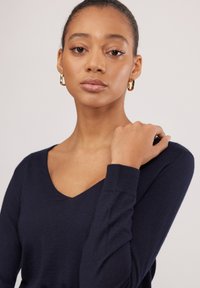 Marineblaues gestricktes Sweatshirt mit V-Ausschnitt, langen Ärmeln und gerippten Bündchen. Die glatte Textur und das figurbetonte Design betonen die Struktur des Kleidungsstücks.