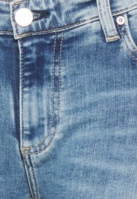 Vaqueros de mezclilla en azul claro con textura desgastada, un botón plateado en la cintura y costuras en contraste a lo largo de las costuras y los bolsillos.