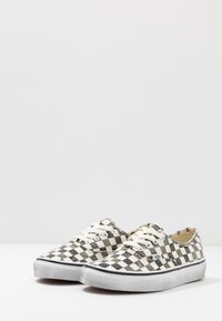 Baskets en toile à carreaux noirs et blancs avec des lacets blancs et des semelles en caoutchouc. Présente le logo Vans sur le côté, un design plat et un bout rond.