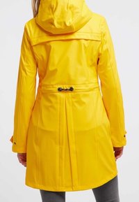 Gul vattentät jacka med huva, åtdragen midja, ryggveck och tryckknappar på ärmarna. Slätt, glänsande material med en figurnära design.