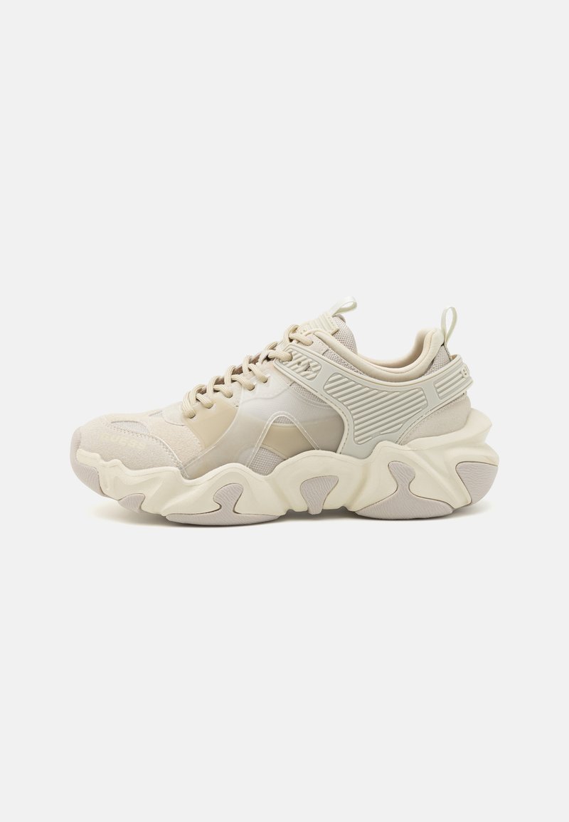 Chunky beige sneakers with a textured mesh upper, rubber sole, and distinct wavy sole design. Features a lace-up closure and heel tab.