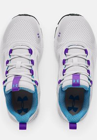 Scarpe atletiche bianche con parte superiore in mesh, dettagli viola e blu, e suola testurizzata. Presentano lacci elastici e un logo sulla linguetta.