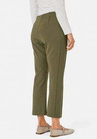 Olijf groene katoenen pantalons met een taps toelopende vorm, voorzien van een hoge tailleband en zijnaad, gecombineerd met lichtgrijze instap schoenen.