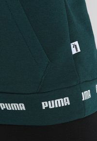 Zelená mikina s kapucí s jemnou texturou, vybavená klokánkovou kapsou a lemem s bílým logem "PUMA". Obsahuje malou cedulku s logem.