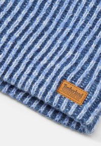 Sciarpa di lana blu con strisce alternate di blu chiaro e blu scuro. Presenta un'etichetta in pelle marrone Timberland cucita. Materiale morbido e contexture.