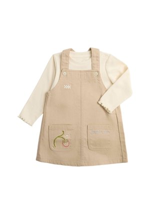 Abito smanicato beige con tasche frontali e dettagli ricamati indossato sopra una camicia a maniche lunghe color crema con polsini smerlati.