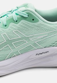 Lichtgroene sportschoen met een textuur van mesh bovenkant, synthetische overlays en een witte zool gemarkeerd met "FlyteFoam." Voorzien van een vetersluiting.