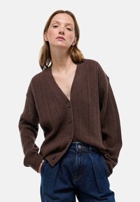 Cardigan marron à côtes avec un décolleté en V, fermeture à boutons et manches amples, associé à un pantalon en denim bleu taille haute.