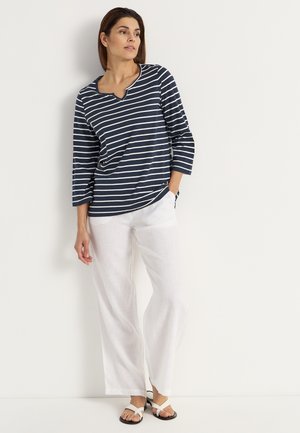 Navy and white striped long-sleeve top with a round neckline, paired with loose white linen pants and black and white sandals.