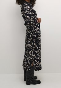 Granatowa sukienka w liściowy wzór w kolorze ecru, z długimi rękawami, prostą sylwetką, bocznymi rozporkami, zestawiona z czarnymi kozakiem do kolan.