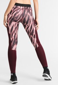Legginsy z różowo-czarnym wzorem zwierzęcym na teksturowanej tkaninie, z jednolitymi burgundowymi sekcjami na dolnej części nogi oraz czarnym pasem w talii.