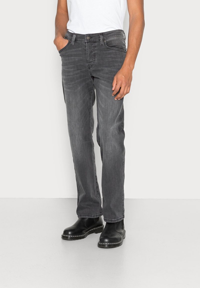 Vaqueros de mezclilla gris con corte recto, diseño de cinco bolsillos y sutil desgaste. Combinados con una camiseta básica blanca y botas negras.