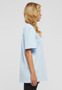 Helles blaues Baumwoll-T-Shirt mit vertikalen weißen Streifen, kurzen Ärmeln und entspannter Passform, getragen mit schwarzen Hosen.