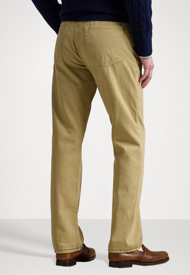 Beige Baumwollhosen im Straight-Leg-Design, mit zwei Gesäßtaschen und dezenten Nähdetails. Kombiniert mit braunen Schuhen.