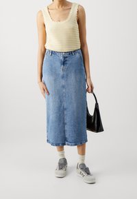 Světle béžový pletený top bez rukávů se zvlněnými lemy, v kombinaci s středně dlouhou modrou džínovou sukní. Doplněno černou kabelkou a šedými teniskami.