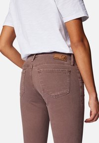 Jeans de algodón marrones con un ajuste de talle medio, que cuentan con bolsillos traseros y una etiqueta de marca de cuero en la cinturilla. Tejido texturizado con un acabado suave.