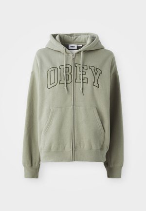 Olīvzaļš džemperis ar rāvējslēdzēju, ar priekšējo kangaroo kabatu, izšūts "OBEY" logotips kontrastējošā tumšākā zaļā krāsā un aukliņu kapuce.