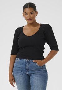 Sort ribbet bluse med V-hals og korte puffede ærmer, parret med lyse denim jeans. Enkel design med en tætsiddende silhuet.