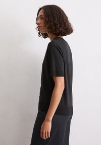 Top nero a maniche corte con vestibilità rilassata, realizzato in tessuto morbido. Presenta un colletto rotondo e una leggera texture a maglia all'orlo.
