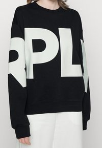 Sudadera negra con grandes letras blancas "RPL" en el frente y detalles blancos en las mangas. El material parece suave, con un ajuste relajado.