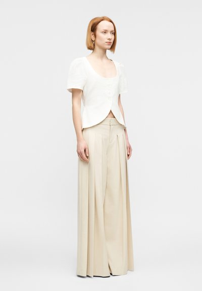 Λευκό λινό μπλουζάκι με κοντά μανίκια, στρογγυλή λαιμόκοψη κα ι κλείσιμο με κουμπιά, συνδυασμένο με μπεζ πλισέ παντελόνι ψηλόμεσο.