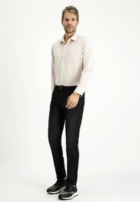 Camicia a maniche lunghe rosa chiaro con tasca, abbinata a jeans neri slim-fit e sneakers nere. Tessuto morbido e design classico.