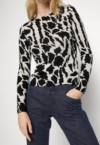 Black and white long-sleeve sweater with abstract animal print; features a rounded neckline and ribbed cuffs; paired with dark jeans.