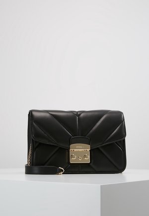 Sac à main en cuir noir matelassé avec fermoir doré et petit détail chaîne, posé sur une surface blanche avec un fond uni.