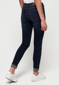 Tammatsu denim farkut kapeä lahkeilla, korkea vyötärö, takataskut ja käännetyt lahkeet, yhdistetty valkoisiin tennareihin.