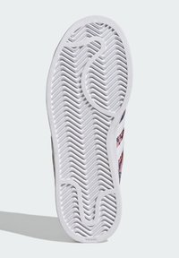 Valge kummist tossu tallaga, millel on laineline mustriga tallamuster. Pealmisel osal on roosad ja sinised aktsendid, kootud disaini ja kontrastsete triipudega.