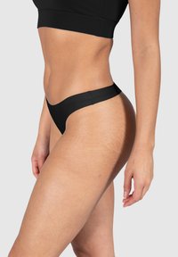 Zwarte string ondergoed met een gladde, elastische textuur en minimale bedekking. Heeft een brede band in de taille voor een veilige pasvorm.