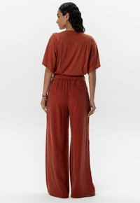 Ensemble bicolore couleur rouille comprenant un haut décontracté à manches courtes et un pantalon évasé. Tissu doux avec une texture lisse.
