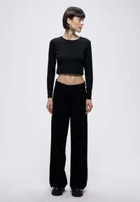 Schwarzes, kurz geschnittenes Langarmshirt kombiniert mit hoch taillierter, schwarzer, weiter Hose. Das Outfit besticht durch ein minimalistisches Design und eine glatte Textur.