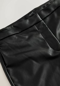 Black faux leather trousers featuring a smooth texture, flat waistband, front pocket details, and a label with 'NEXT' on the waistband.