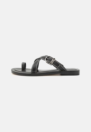 Black leather sandals with a cross strap design, featuring a silver buckle and white stitching. Flat sole, open-toe style, minimalist aesthetic.